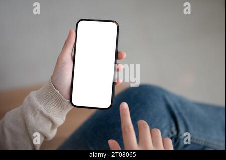 Immagine ravvicinata di una donna seduta al chiuso e che utilizza lo smartphone, toccando sullo schermo. Un modello di smartphone con schermo bianco nella mano di una donna. sms, m Foto Stock