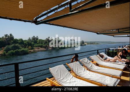 Vista dal ponte di una piccola nave da crociera sul nilo, adornata con sedie per prendere il sole, che offre uno scorcio del maestoso ecosistema del nilo. Foto Stock