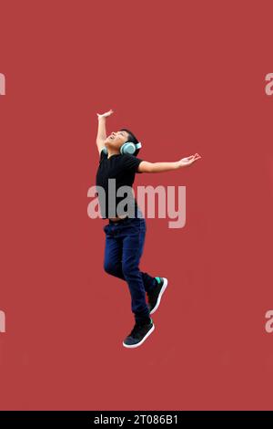 Un latinoamericano di 9 anni dalla pelle scura salta felicemente mentre ascolta la musica con le cuffie Foto Stock