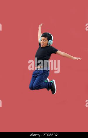 Un latinoamericano di 9 anni dalla pelle scura salta felicemente mentre ascolta la musica con le cuffie Foto Stock