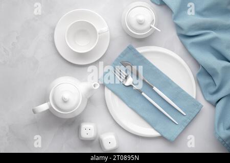 Piatti in ceramica bianca e posate in argento. Coltello, forchetta e tovagliolo blu su sfondo grigio. Il tè beve la mattina. Impostazione tavolo, piano, bordo superiore Foto Stock