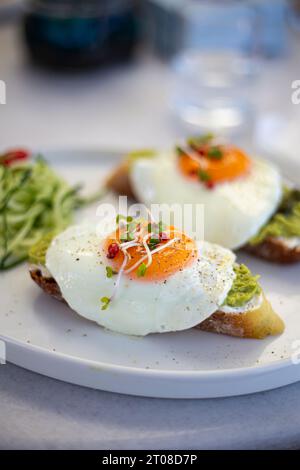 Gustosi e bellissime uova alla benedict fritte servite con toast all'avocado per colazione da vicino Foto Stock