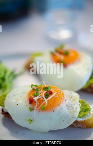 Gustosi e bellissime uova alla benedict fritte servite con toast all'avocado per colazione da vicino Foto Stock