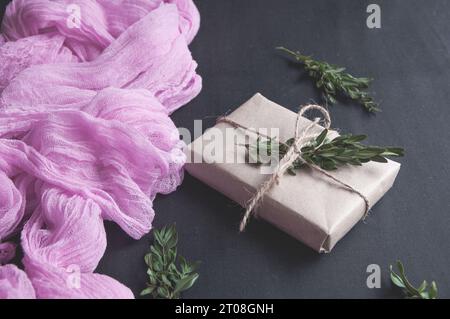 Natale avvolto o altro regalo natalizio fatto a mano in carta kraft con spago e ramoscello di pino su sfondo rosa Foto Stock