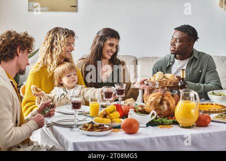 Felice afro-americano che passa panini al forno agli amici durante la cena del giorno del Ringraziamento, il giorno del tacchino Foto Stock