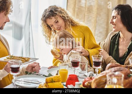 Una famiglia allegra e multirazziale che gusta una deliziosa cena mentre si riunisce il giorno del Ringraziamento con tacchino arrosto Foto Stock