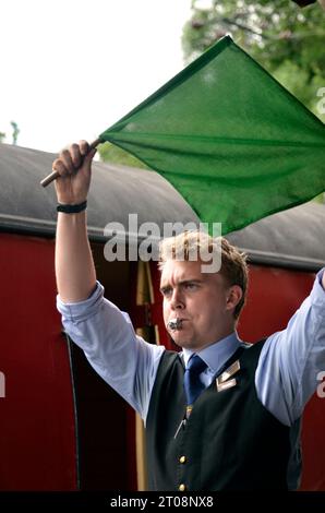 la guardia alza la bandiera e fa fischiare il treno per partire, weybourne, nord norfolk, inghilterra Foto Stock