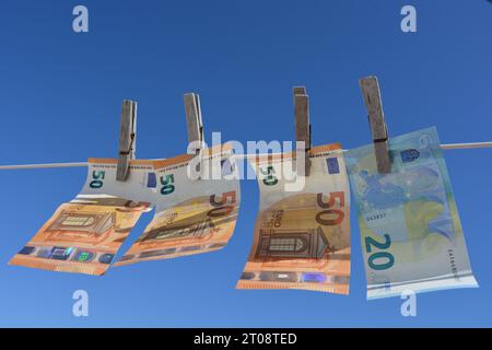 Banconote europee appese su una linea di lavaggio con vecchi vestiti di legno poggiati contro il cielo blu. Concetto creativo, riciclaggio di denaro Foto Stock