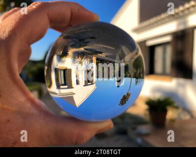 Sfera di cristallo in mano, fotografia rifrazione, guardando attraverso l'obiettivo una villa al sole Foto Stock