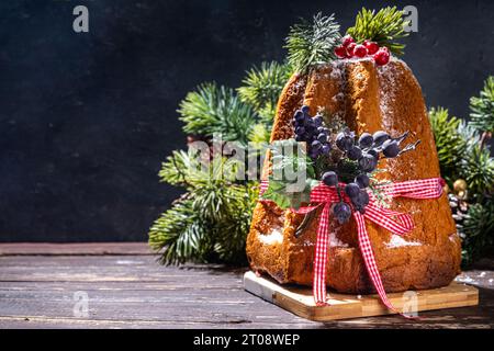 Tradizionale torta di frutta di Natale italiana Panettone Pandoro con festoso nastro rosso e decorazioni natalizie, su sfondo di legno scuro, spazio copia Foto Stock