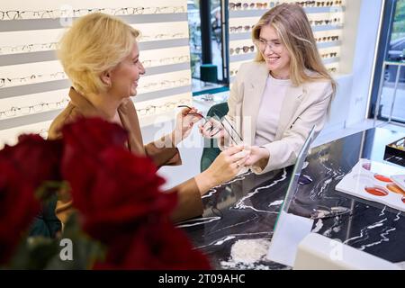 Una donna di mezza età prova con occhiali diversi in un salone di ottica Foto Stock