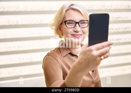 La signora in una blusa marrone si fa un selfie indossando occhiali nuovi Foto Stock