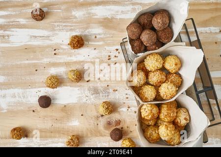 Vista dall'alto di Sweet panellets in coni di carta da giornale in cestino nero su un tavolo di legno marrone e bianco Foto Stock