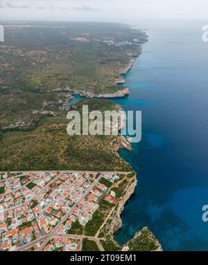 Dall'alto, vista con droni dell'incredibile laguna turchese, litorale dell'isola di Minorca con case da resort e vegetazione Foto Stock