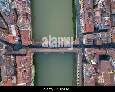 Vista aerea dall'alto verso il basso del ponte sul fiume Arno nella città di Firenze, con stradine strette e case residenziali con tetti arancioni piastrellati nella città vecchia in giornata Foto Stock