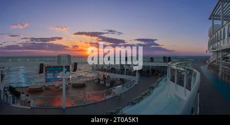 Catturato dalla prua di una nave da crociera, il tramonto sulla Sardegna si svolge in uno spettacolo di colori vivaci. Le tranquille acque del mirr mediterraneo Foto Stock