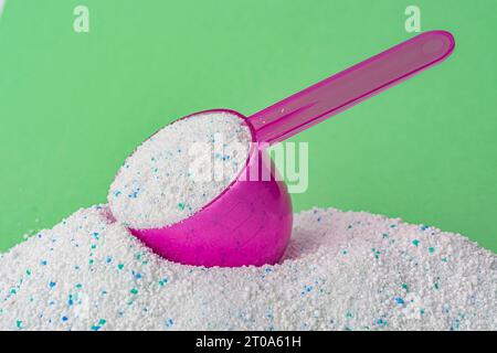 Detersivo in un cucchiaio di plastica su sfondo verde. Foto di alta qualità Foto Stock