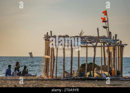 Capanna dei pescatori con reti da pesca sulla spiaggia principale di Negombo in Sri Lanka con una famiglia che gironzola intorno alla barca al tramonto Foto Stock