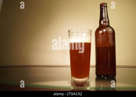 Una bottiglia di birra marrone e un bicchiere da pinta - un simbolo della passione per la birreria artigianale. Luce parassita sullo sfondo. Sufficiente per il posizionamento del testo a sinistra. Foto Stock