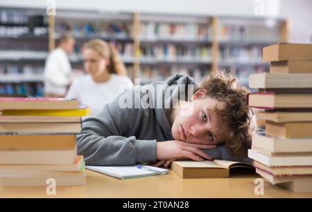 Ragazzo adolescente stanco in biblioteca Foto Stock