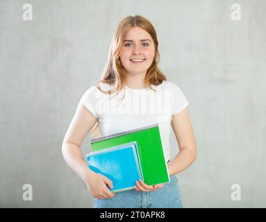 Ritratto di ragazza felice adolescente in abbigliamento casual tenendo a spirale e sorridendo alla macchina fotografica contro cemento sfondo grigio parete Foto Stock