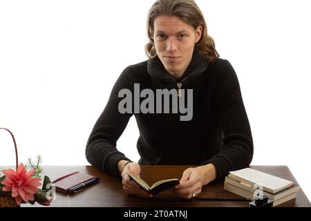 Uno studente siede a un tavolo e legge un libro Foto Stock
