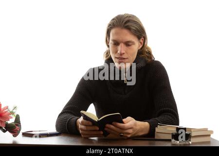 Uno studente siede a un tavolo e legge un libro Foto Stock