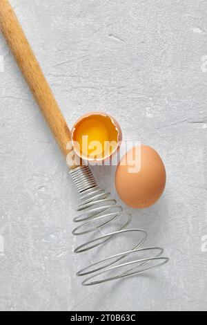 Frusta a spirale e due uova beige crude con tuorlo su un tavolo di cemento leggero. Vista superiore con spazio di copia. Foto Stock