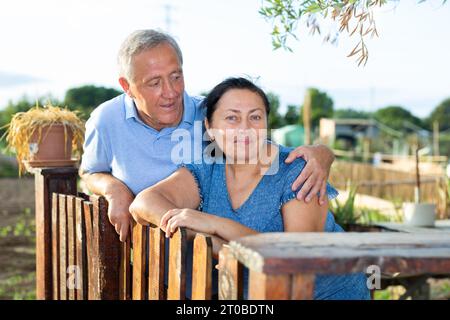 Una coppia più anziana e felice che si trova vicino a una recinzione di legno in una piccola tenuta Foto Stock