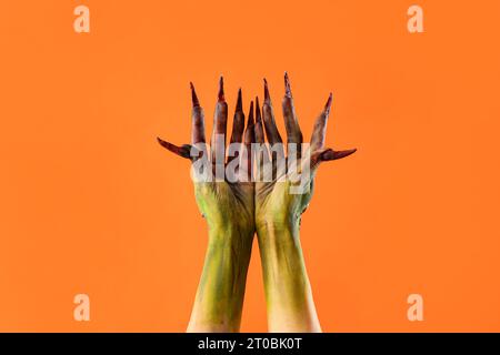 Mani di strega con artigli su sfondo arancione. Festa di Halloween Foto Stock