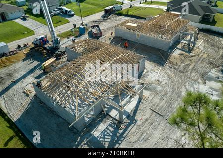 Gru di sollevamento camion e costruttori che lavorano sulla costruzione di tetti di casa residenziale incompiuta con struttura a telaio in legno nella zona suburbana della Florida. Ho Foto Stock