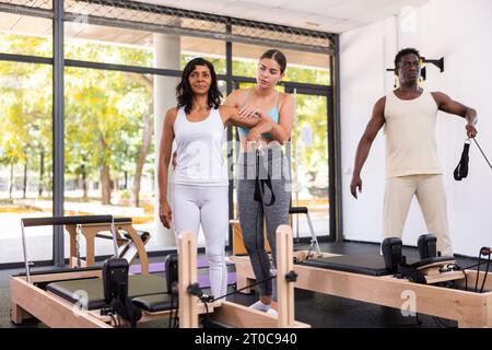 Istruttrice di pilates femminile ispanica che aiuta la giovane donna a fare esercizi sull'apparato riformatore Foto Stock