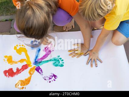 Stampe colorate di mani e piedi dipinti per bambini. Fratello, sorella. amici che si divertono e creano idee creative. Interessante infanzia felice Foto Stock