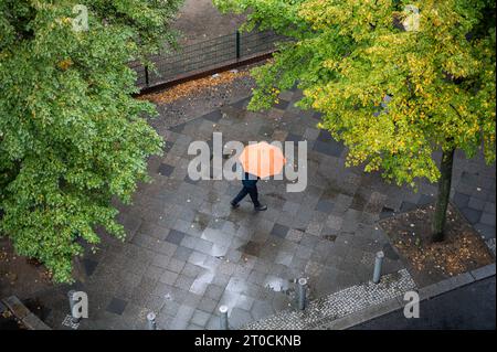 05.10.2023, Berlino, Germania, Europa - persona che tiene un ombrello cammina lungo una strada bagnata in un giorno di pioggia autunnale nel quartiere berlinese di Charlottenburg. Foto Stock