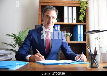 Uomo d'affari che lavora nel suo ufficio con documenti in mano in un ufficio con mobili in legno Foto Stock