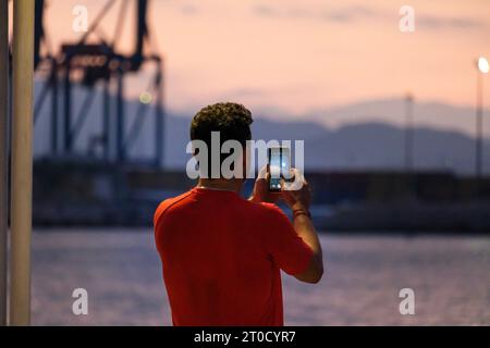 promenade, Malaga, Sunrise, uomo che scatta foto con il cellulare sulla schiena, t-shirt rossa Málaga, Sunrise, uomo che scatta foto con il suo cellulare sul suo b Foto Stock