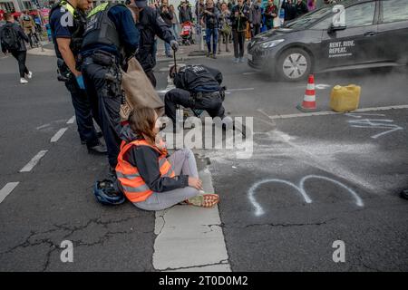 Berlino, Germania. 6 ottobre 2023. Gli attivisti climatici del gruppo ''Letzte Generation'' (Last Generation) nella disobbedienza civile si sono incollati e cementati sulla strada a Potsdamer Platz a Berlino il 6 ottobre 2023, causando significative interruzioni del traffico. La ''generazione Letzte'', nota per i loro metodi di protesta non convenzionali, mira a spingere i governi ad aderire agli obiettivi dell'accordo di Parigi, principalmente l'obiettivo a 1,5 gradi. La polizia, nel tentativo di liberare gli attivisti dalle strade, ha fatto ricorso all'olio da cucina e alle seghe circolari. Anche le conseguenze giuridiche hanno seguito il loro prot Foto Stock