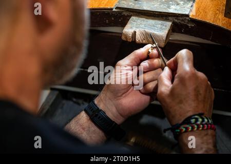 Goldsmith lavora e crea nel suo laboratorio di gioielli d'oro. Gioielliere che infila un gioiello d'argento. Foto Stock