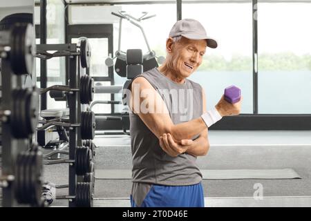 Uomo anziano in abbigliamento sportivo con dolore al gomito che si esercita con un manichino in palestra Foto Stock