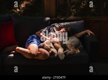 Ragazzo e cane peloso sdraiati insieme in una toppa soleggiata sul divano. Foto Stock