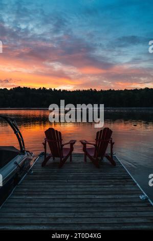 Due sedie adirondack alla fine del molo sul lago all'alba. Foto Stock