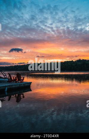 Due sedie adirondack alla fine del molo sul lago all'alba. Foto Stock