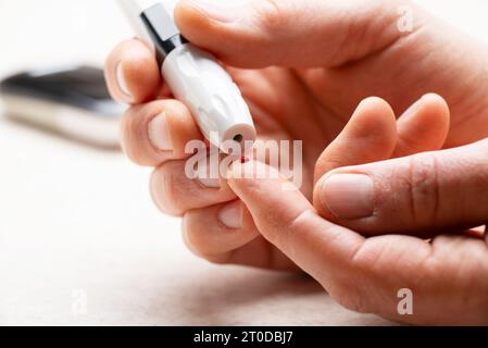 L'uomo caucasico di mezza età ha perforato il dito per il test del glucosio domestico con misuratore e accessori sullo sfondo Foto Stock