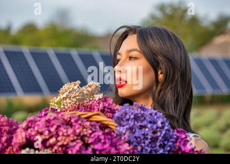 Bella giovane bruna donna caucasica con mazzi di fiori lilla, primo piano. Pannelli solari sullo sfondo. Foto Stock