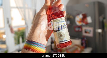 Parigi, Francia - 12 giugno 2023: Vista ravvicinata di una mano maschile con una bottiglia di aperitivo Monin, emblematico del marchio francese specializzato in sciroppi e liquori per locali commerciali Foto Stock