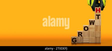Guanti disposti a mano in blocchi di legno con testo in crescita su sfondo arancione e giallo con spazio per la copia. Foto Stock