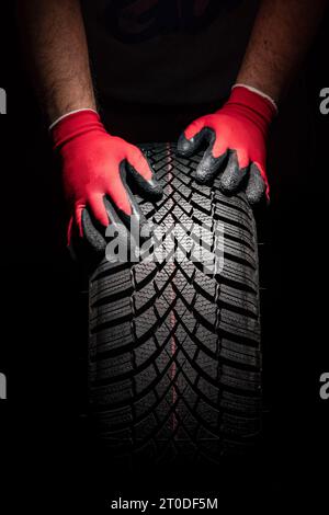 Assistenza pneumatici auto e mani del meccanico che tiene nuovo pneumatico su sfondo nero con spazio per la copia per il testo Foto Stock