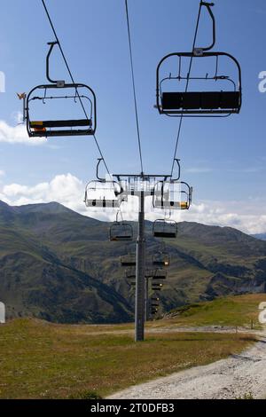 Una seggiovia vuota in estate, in alto nel paesaggio montano e sullo sfondo blu del cielo. Stazione sciistica Valloire in Francia. Copia spazio sottostante. Foto Stock