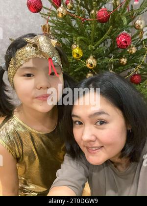 Avvolta in Golden Magic: La mamma e la figlia asiatica catturano la gioia in un selfie di Natale Foto Stock