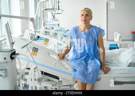 Lady in abito d'ospedale siede sul letto in unità di terapia intensiva Foto Stock